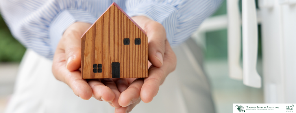 Mains tenant une maison en bois, symbolisant l'achat et la vente de propriétés à Lloret de Mar avec l'agence immobilière Gabinet Senia Associats.